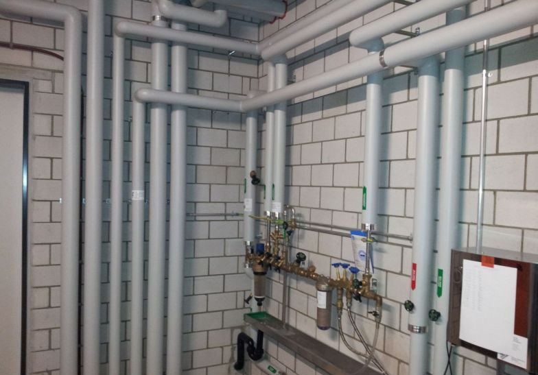 Technikraum mit gedämmten Leitungen und Armaturen an einer Backsteinwand